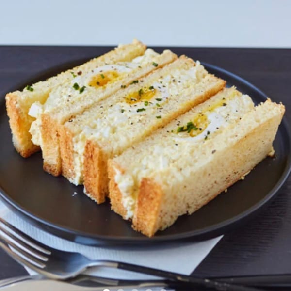 Three egg salad sandwiches with sunny-side-up eggs and chives on a black plate.