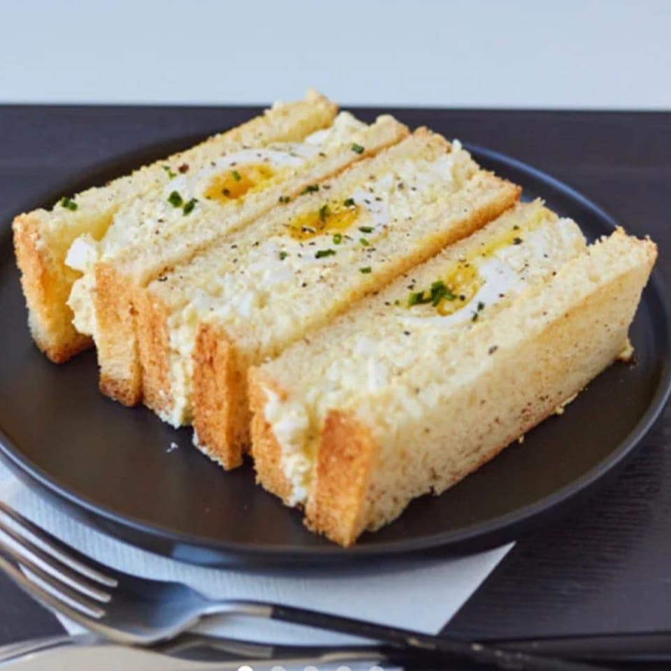 Three egg salad sandwiches with sunny-side-up eggs and chives on a black plate.
