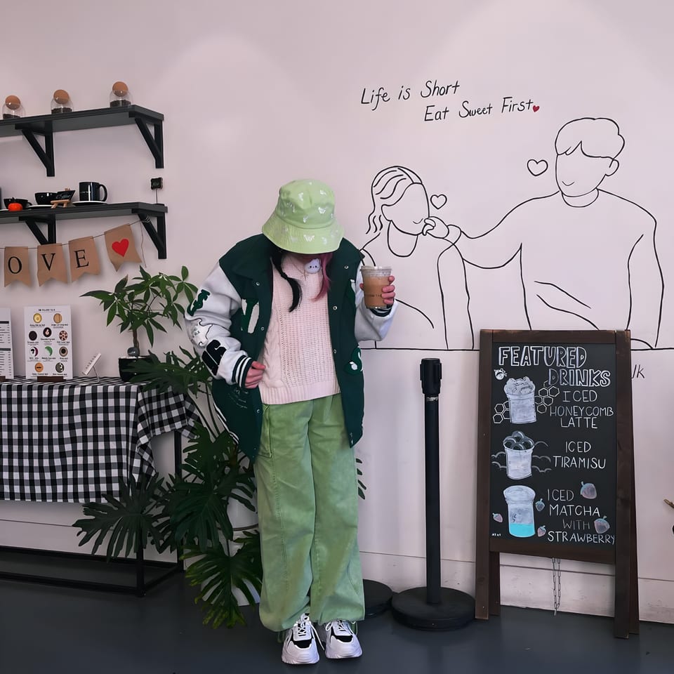 A person in a green bucket hat and jacket holds a drink in the Pillow Talk Cafe.