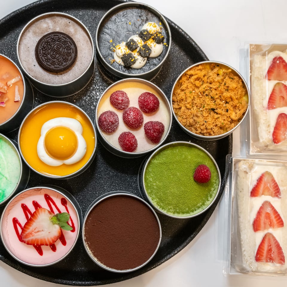 Assortment of Pillow Talk Cafe desserts in round tins, including Oreo, matcha, raspberry, and strawberry sandwiches.