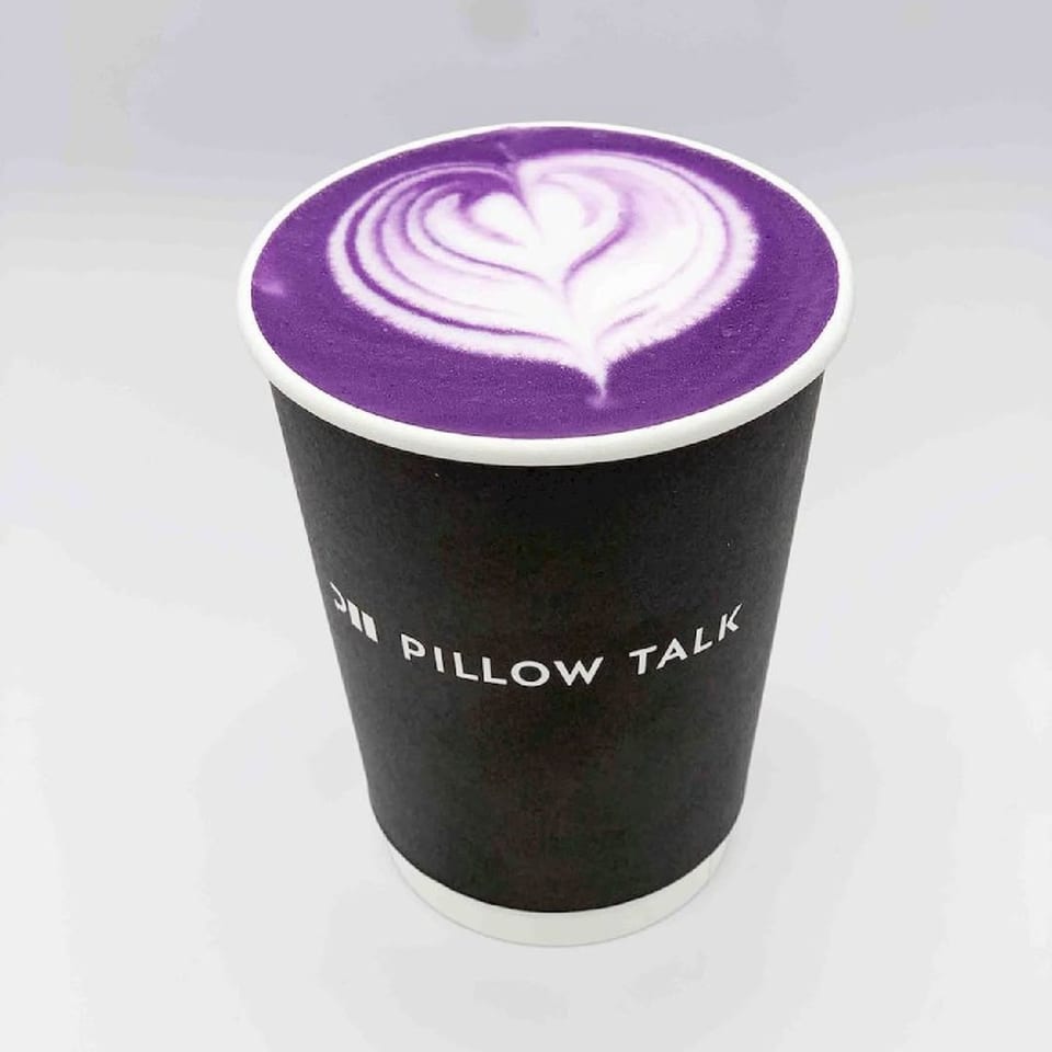 Pillow Talk Cafe's purple latte with white latte art in a black branded cup.