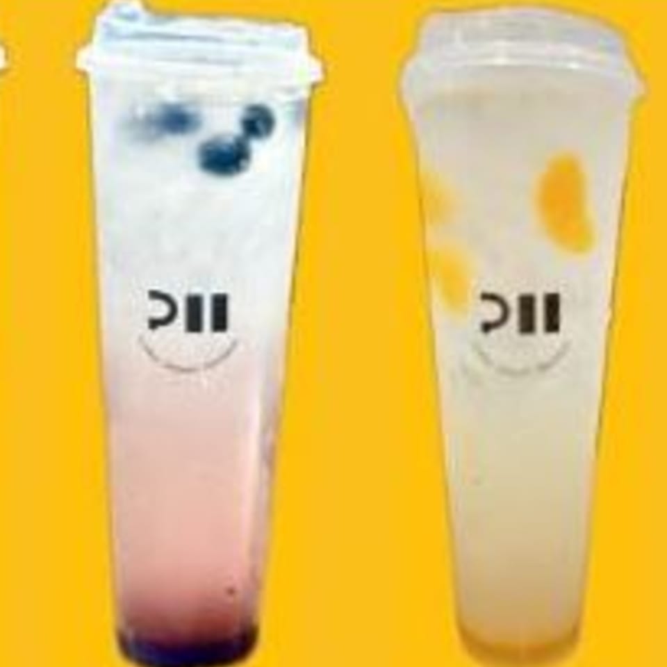 Two clear plastic cups with Pillow Talk Cafe's logo, one with blueberries, the other with mango pieces.