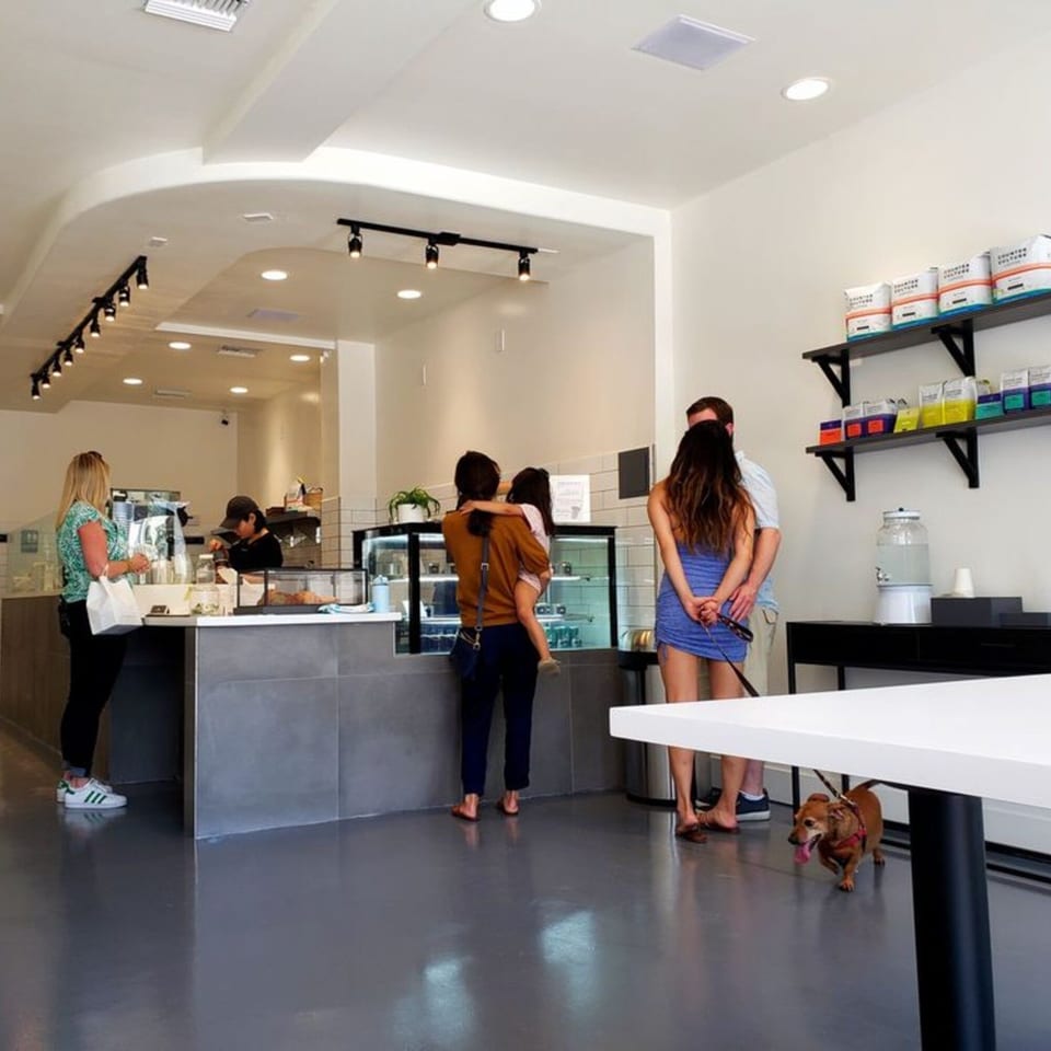 Customers and a dog wait at the counter of Pillow Talk Cafe Pasadena, a bright, modern cafe.