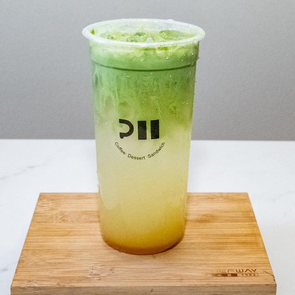 A Pillow Talk Cafe matcha lemonade drink, green on top and yellow on bottom, on a wooden board.