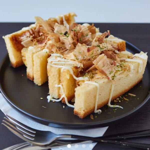 Thick-cut toast slices topped with bonito flakes, mayonnaise, and green herbs on a black plate.