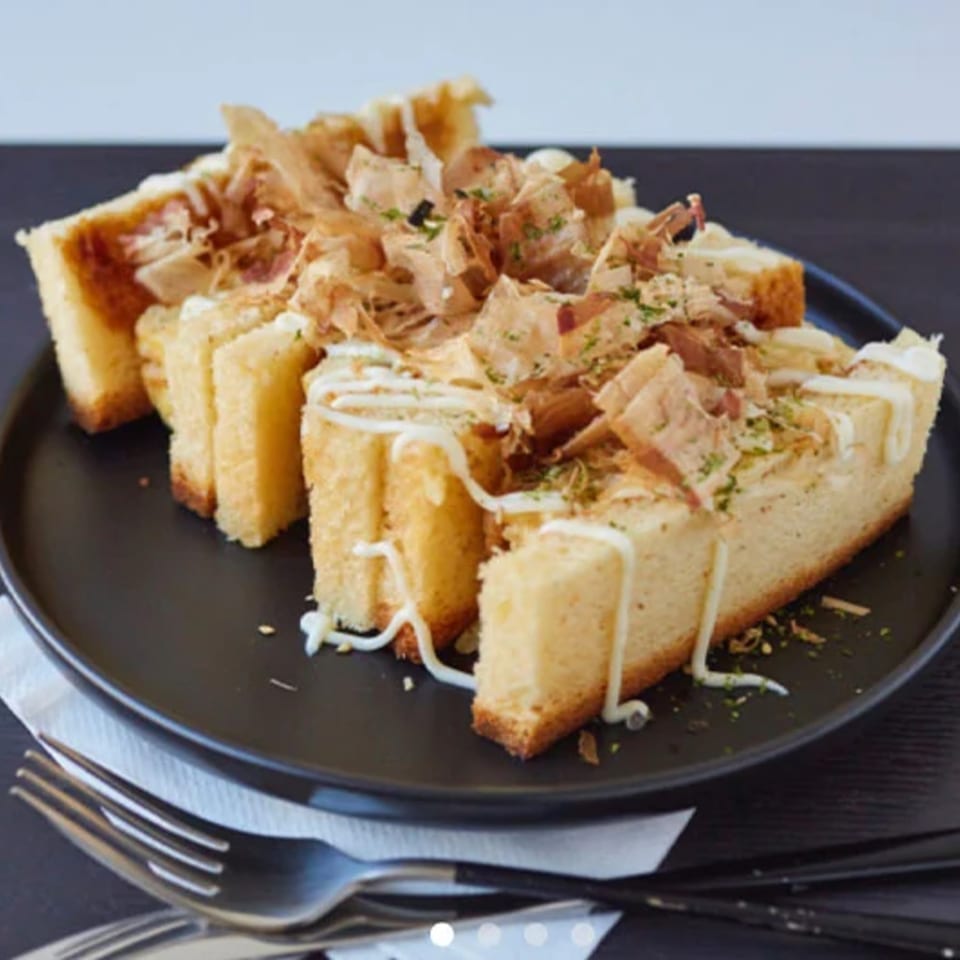 Thick-cut toast slices topped with bonito flakes, mayonnaise, and green herbs on a black plate.