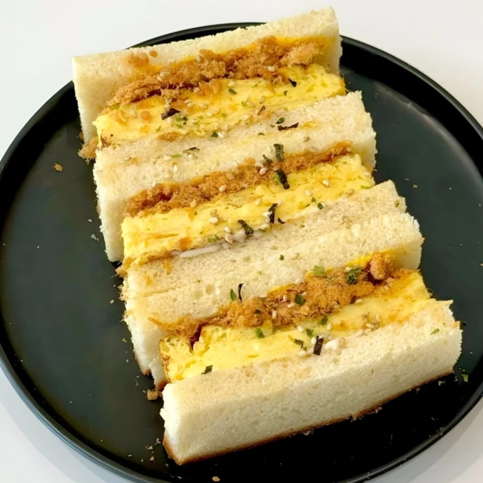 Pillow Talk Cafe's egg and pork floss sandwich, cut into triangles, on a black plate.