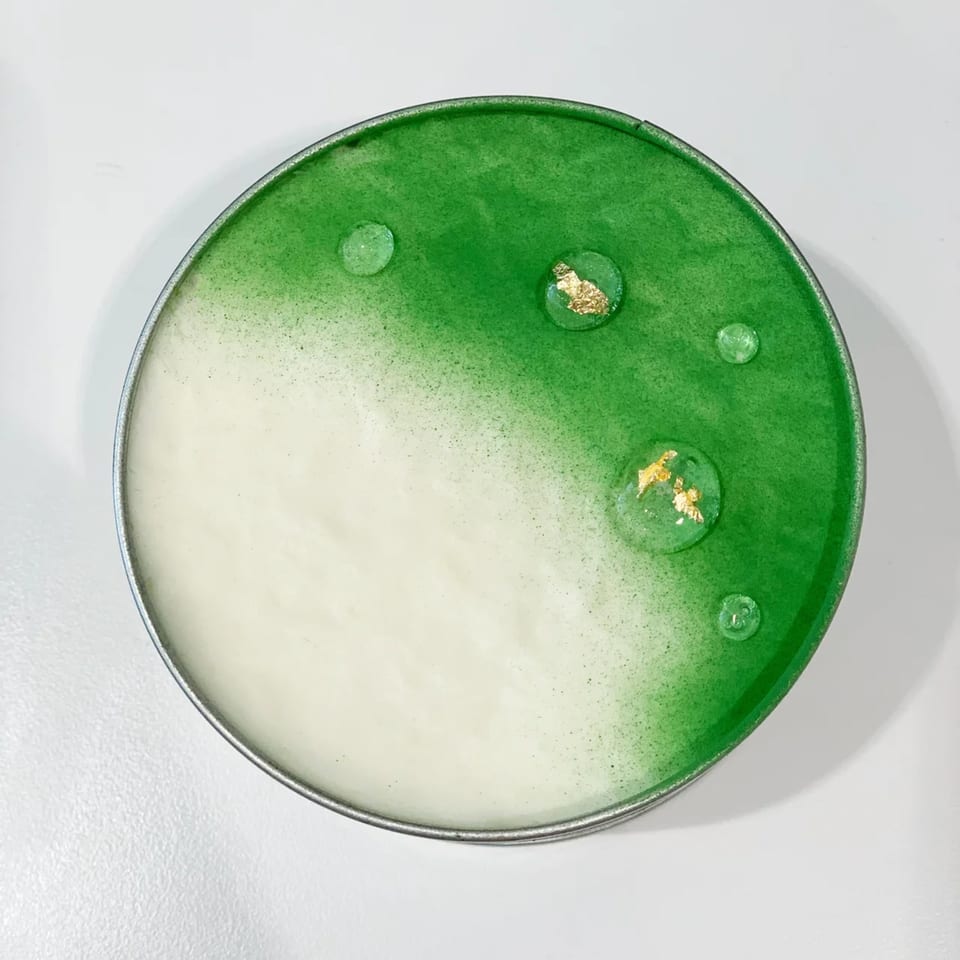 Round dessert with a gradient from white to green, topped with clear drops and gold flakes.