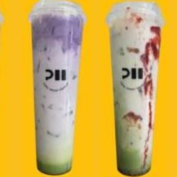 Two tall plastic cups of layered drinks, one purple and green, the other red and green.