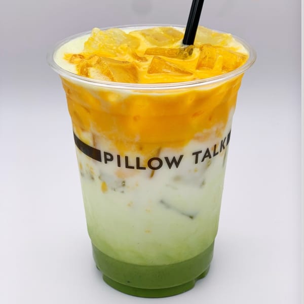 A vibrant layered drink from Pillow Talk Cafe with green, white, and orange layers, ice, and a black straw.