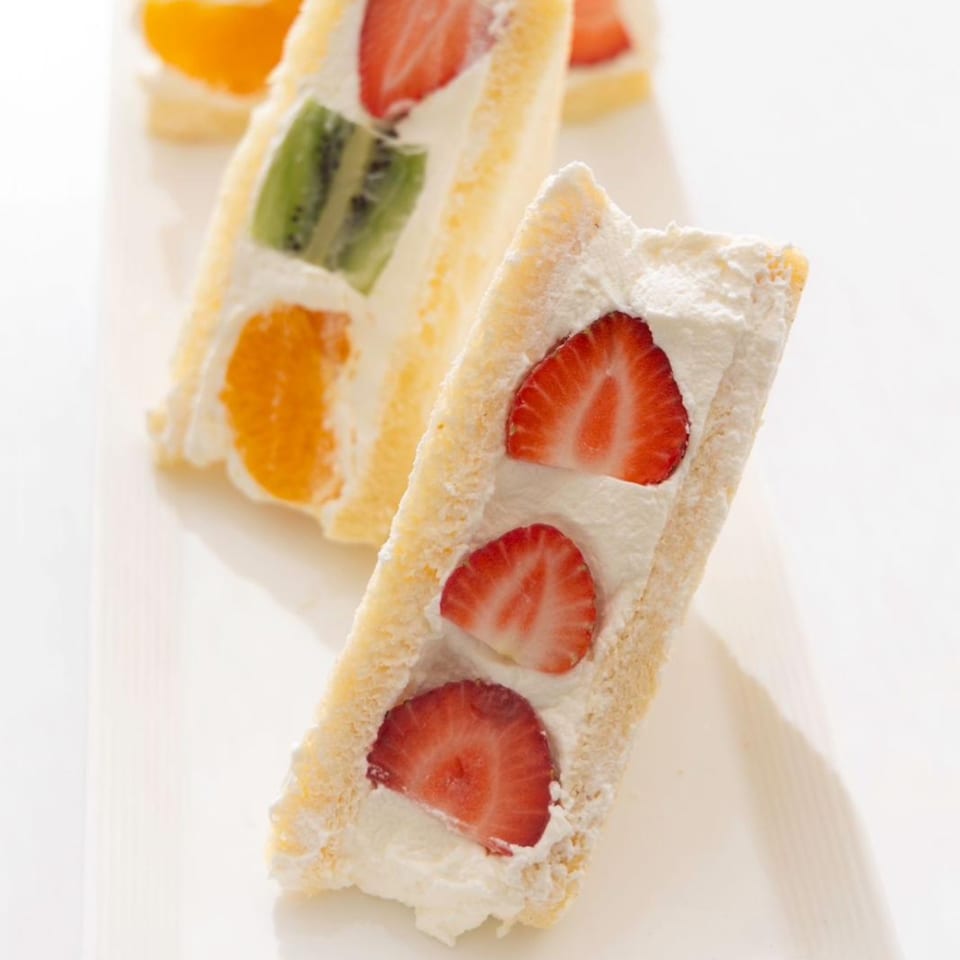 Sweet fruit sandwiches with whipped cream and various fruits, including strawberries, kiwi, and oranges.