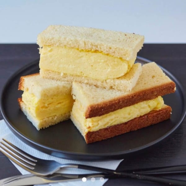 Three fluffy egg salad sandwiches on white bread, served on a dark plate with cutlery.