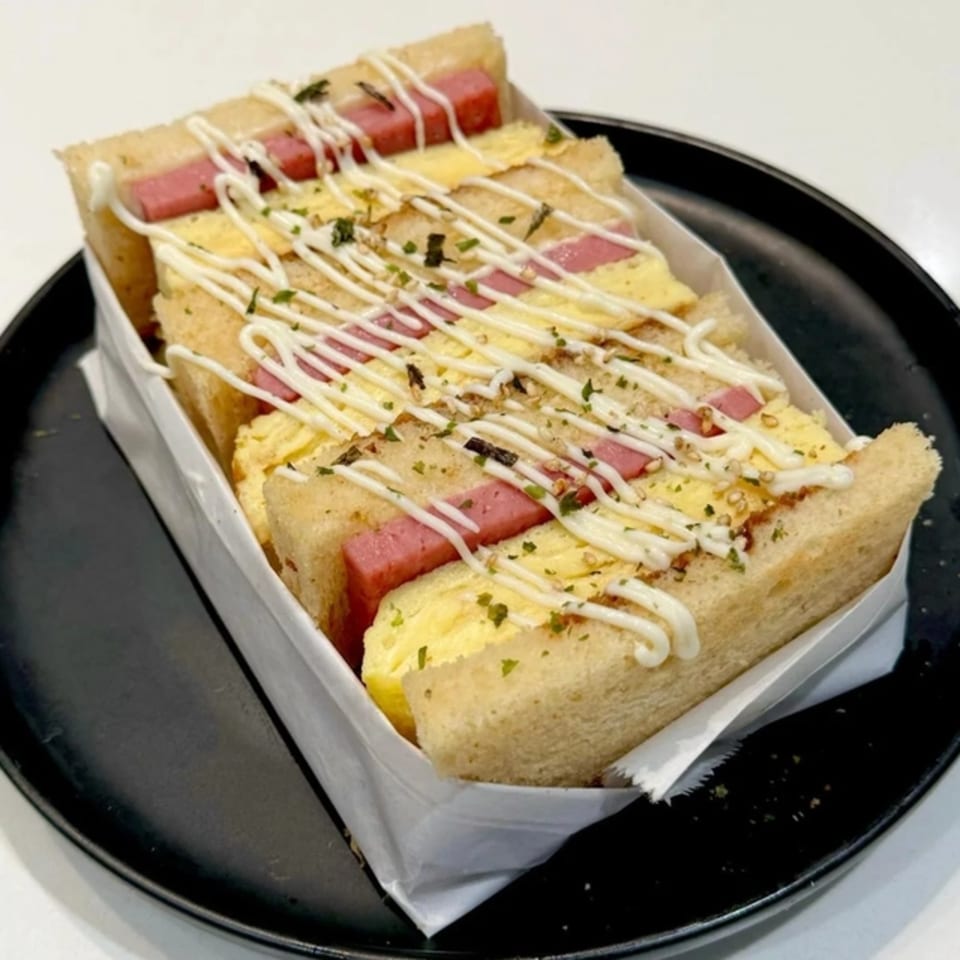 Pillow Talk Cafe's spam and egg sandwich, drizzled with mayonnaise and herbs, on a black plate.